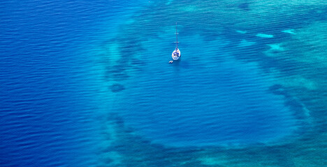 White yacht floating above a coral reef in beautiful bay. Aerial view.