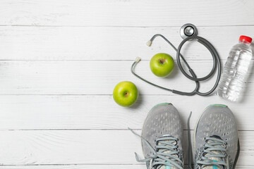 Running shoes with green apples and stethoscope near  fresh water bottle