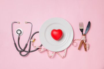 Red heart white plate and stethoscope with measuring tape around fork and knife