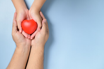 adult and child hands holding red heart isolated on blue background,