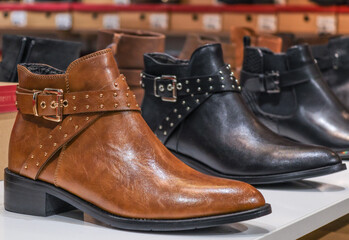 one pair of brown ankle boots.
One pair of brown boots along with black ones lie in a row on a shelf, close-up side view.