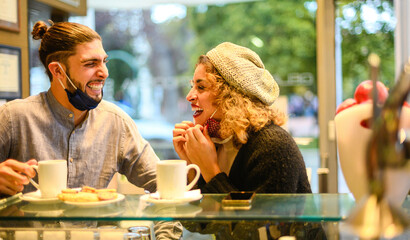Beautiful happy loving couple with face mask enjoying breakfast in a cafe in the coronavirus time