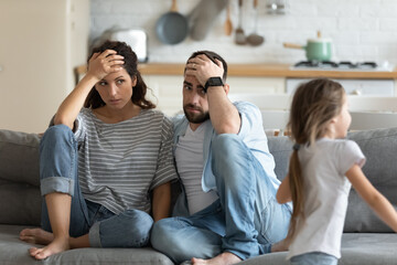 Tired mother and father having problem with noisy naughty daughter shouting and running around sofa...