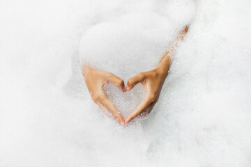Woman hands in heart shape in bath full of foam bubbles close-up. Spa beauty treatment. Love symbol
