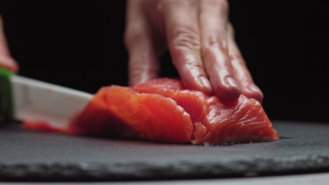 Sushi Chef Slices fresh Salmon on the sushi bar. Chef cutting salmon fillet at professional kitchen. Closeup chef hands slicing fresh fish slice in slow motion. Professional man cutting red fish