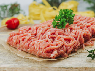 raw minced meat on a wooden board.
Raw minced meat with herbs and cherry tomato on baking paper, close-up side view.