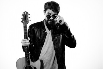 A man holds a guitar in his hands black leather jacket dark glasses music performance light background