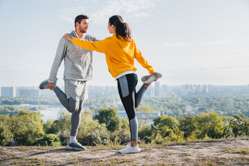 Two young male and female athletes exercising together in the morning against urban background