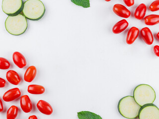 vegetables on a white background.
Cherry tomatoes and sliced ​​zucchini around the edges on a white plate with space for text in the middle, top view close-up.

