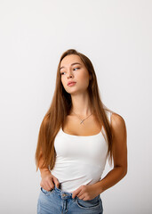 A beautiful young slender long haired brunette girl holds her jeans and looks thoughtfully to the side. The concept of healthy food, diet, lifestyle. Studio photo on white background