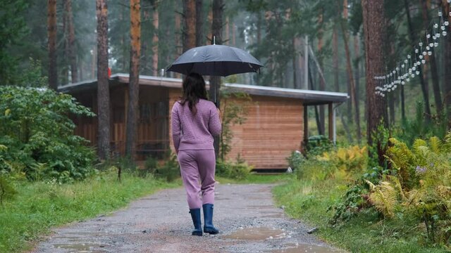 Woman in Blue Rubber Boots with Umbrella Enjoying Walking in the Rain in Nature. Back View. Autumn Season, Harmony with Nature and People concept