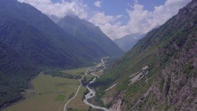 Huge majestic mountains of the North Caucasus with a turbulent river at the bottom of the gorge. Aerial shot. Sunny day. Mountains, peaks, cliffs, rocks, ridges, landscape, green grass, sky, clouds