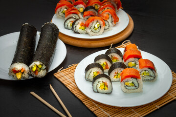 A variety of sushi roll with salmon, avocado and cucumber on a black table. Sushi menu. Japanese food.