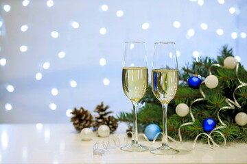 Two glasses of champagne composition with Christmas and new year decorations on a blurry background of burning garlands