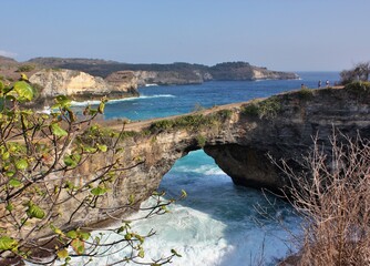 Fototapeta na wymiar Scenic natural arch with plants in foreground at Broken Beach, Nusa Penida, Indonesia