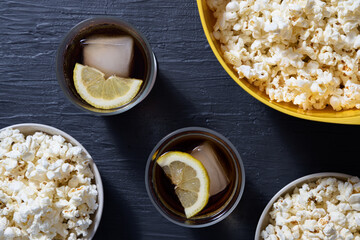 Bowl with popcorn and glasses of iced cola on blue background. Top view
