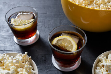 Bowl with popcorn and glasses of iced cola on blue background. Perspective