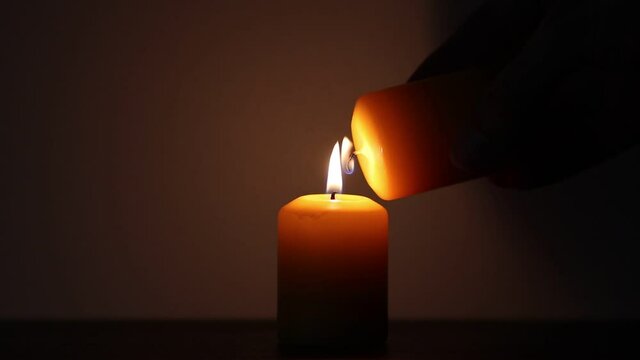 Hand lighting up a candle with another candle on a dark background. Religion and spirituality concepts
