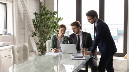 Focused young business people looking at computer screen, discussing electronic financial or marketing research report. Skilled leader showing project presentation, explaining software to colleagues.