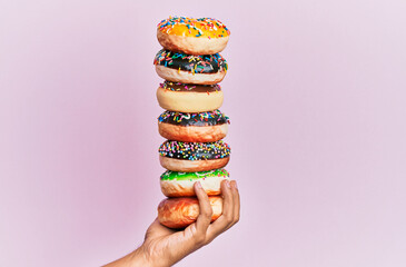 Hand of hispanic man holding tower of donuts over isolated pink background.