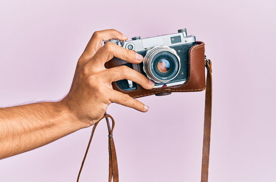 Hand of young hispanic man holding vintage camera over isolated pink background.