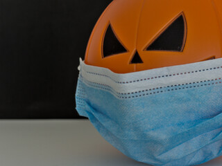 Close up view of Halloween pumpkin lantern wearing a medical facial mask as a symbol of disease control and virus infection and coronavirus or covid-19 with black background. Selective focus