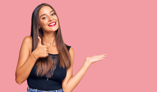 Young hispanic woman wearing casual clothes showing palm hand and doing ok gesture with thumbs up, smiling happy and cheerful