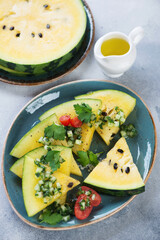 Slices of yellow watermelon topped with herbed chopped cucumber and served on a turquoise plate, vertical shot