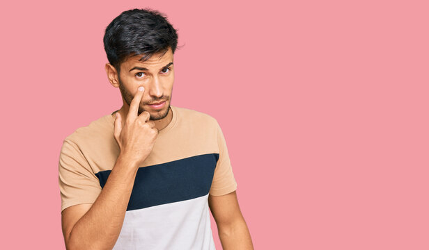 Young handsome man wearing casual clothes pointing to the eye watching you gesture, suspicious expression