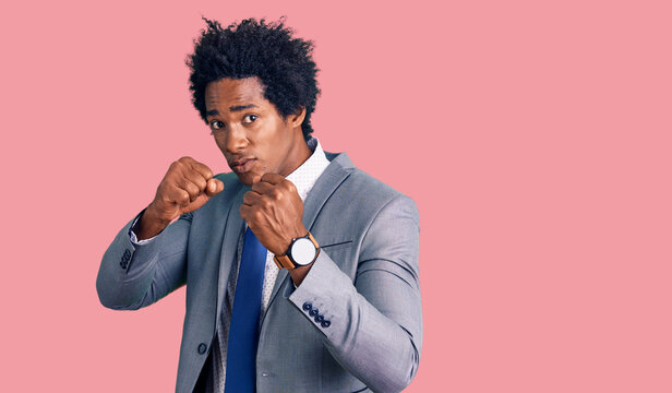 Handsome african american man with afro hair wearing business jacket punching fist to fight, aggressive and angry attack, threat and violence