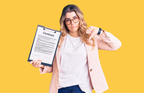 Young caucasian woman holding clipboard with contract document with angry face, negative sign showing dislike with thumbs down, rejection concept