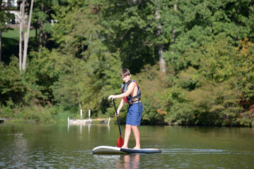 Fototapeta na wymiar Boy standing up on a paddleboard on calm lake