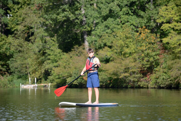 Fototapeta na wymiar Boy standing up on a paddleboard on calm lake