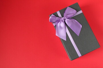 new year's Christmas holiday mother's day Valentine's day birthday anniversary gift box black with purple purple fuchsia colors with a bow on a red background copy space