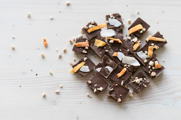Milk vegan chocolate with coconut and pieces of dried mango on a white wooden background