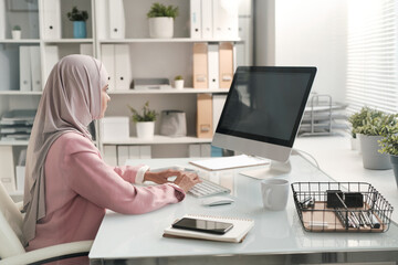 Contemporary serious Muslim businesswoman working with online data in office