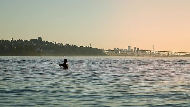 Silhouette of a man in the ocean with a fishing rod with Vancouver in the background at sunset. HD 24FPS.
