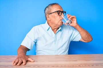 Handsome senior man sitting on the table at home drinking a glass of fresh water