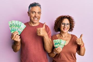 Beautiful middle age couple holding south african 10 rand banknotes smiling happy and positive,...