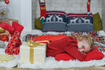 Cute little girl lying on the carpet. Christmas tree in the background. smiles. Beautiful little girl in the bright New Year's interior