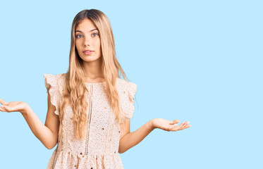 Beautiful caucasian woman with blonde hair wearing elegant summer clothes clueless and confused expression with arms and hands raised. doubt concept.