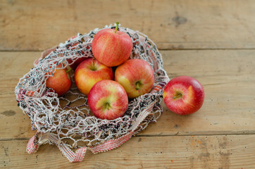Red apples are in fishnet on wooden table