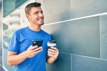 Young caucasian man using smartphone and drinking take away coffee at the city.