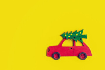 toy wooden red car with Christmas tree on the roof on yellow background