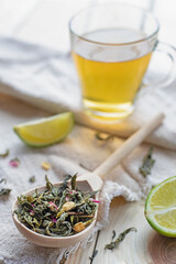 green tea leaves in a wooden spoon on linen textiles with lime slices and mug of brewed tea