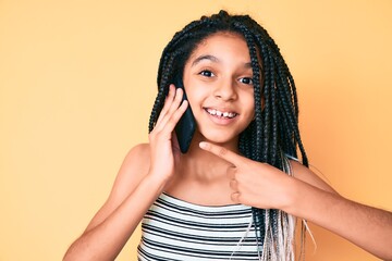 Young african american girl child with braids having conversation talking on the smartphone smiling happy pointing with hand and finger