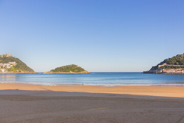 Fototapeta na wymiar San Sebastian, Spain - 10/11/2019: Seashore with unknown people. Wide aerial beach in morning sunlight. People walking on coast of Biscayne bay. Healthy and relax lifestyle. Scenic seascape in morning