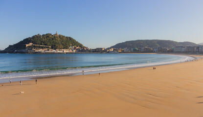 People walking with dogs on the beach called La Concha. Tourists in bay of Biscay in San Sebastian in autumn. Wide aerial beach in morning sunlight. Healthy and relax lifestyle. San Sebastian landmark