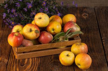 apples in a box on a wooden table and a bouquet of autumn flowers