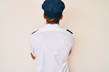 Young hispanic man wearing airplane pilot uniform standing backwards looking away with crossed arms
